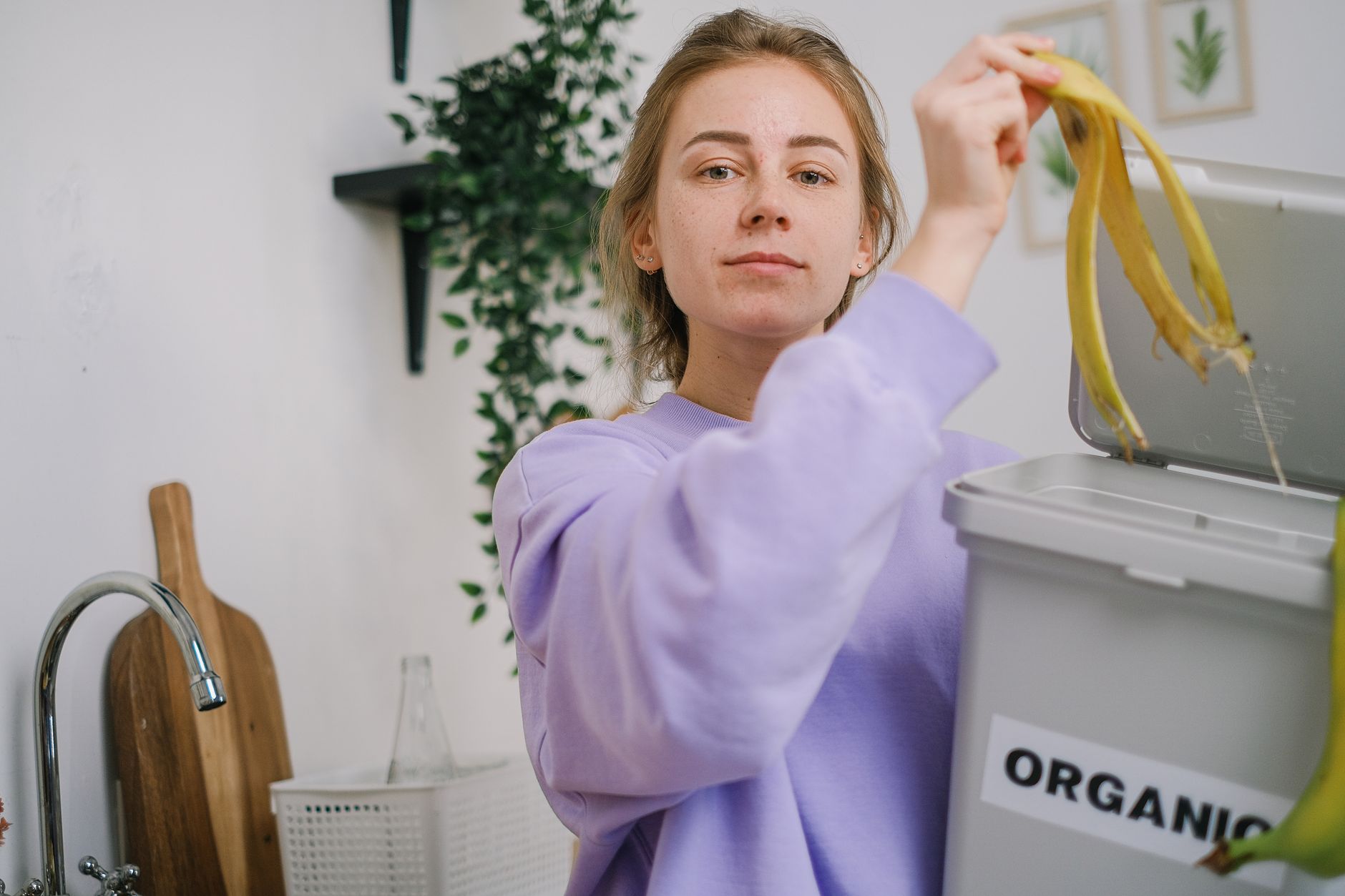 A smiling person holding a reusable water bottle while planting a seedling, illustrating sustainable habits that truly stick.